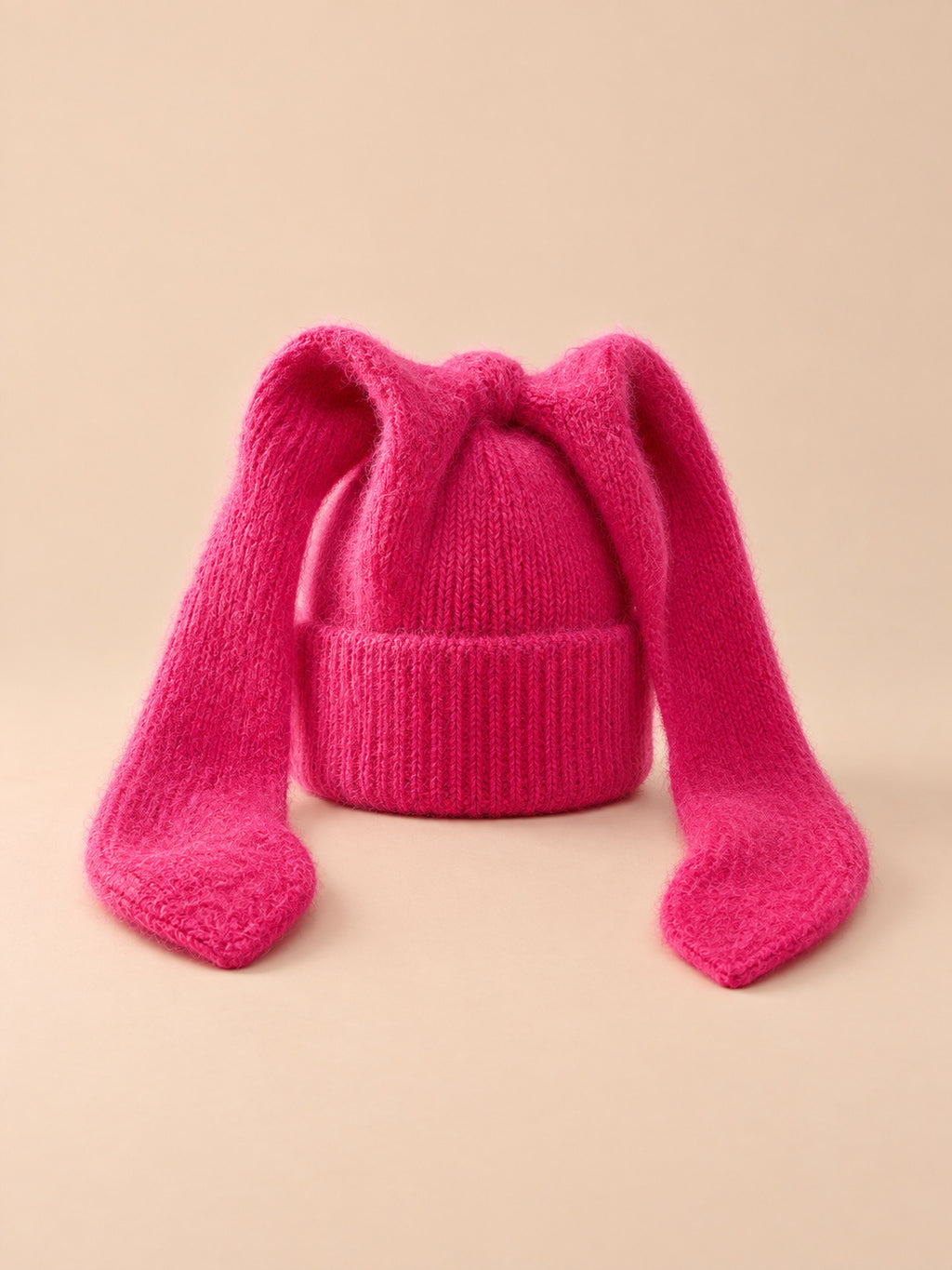 Bonnet à oreilles de lapin, rouge, vue de face sur fond pêche sable.