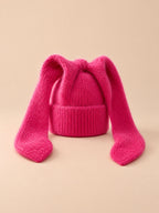 Bonnet à oreilles de lapin, rouge, vue de face sur fond pêche sable.