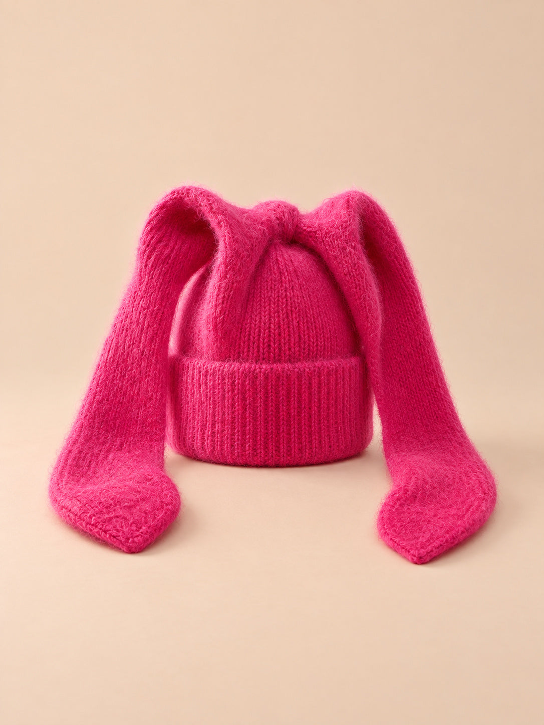 Bonnet à oreilles de lapin, rouge, vue de face sur fond pêche sable.