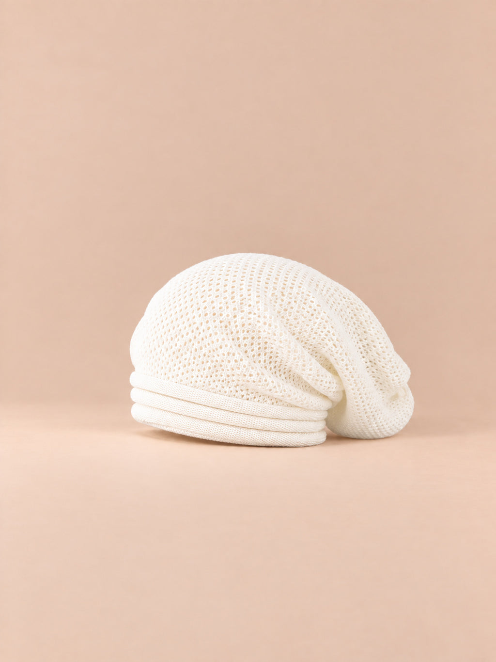 Bonnet oversize en maille blanc, vue de trois quarts sur fond pêche sable.