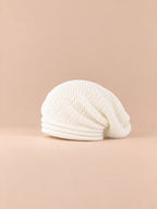 Bonnet oversize en maille blanc, vue de trois quarts sur fond pêche sable.