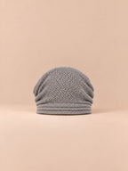 Bonnet oversize en maille gris clair, vue de face sur fond pêche sable.