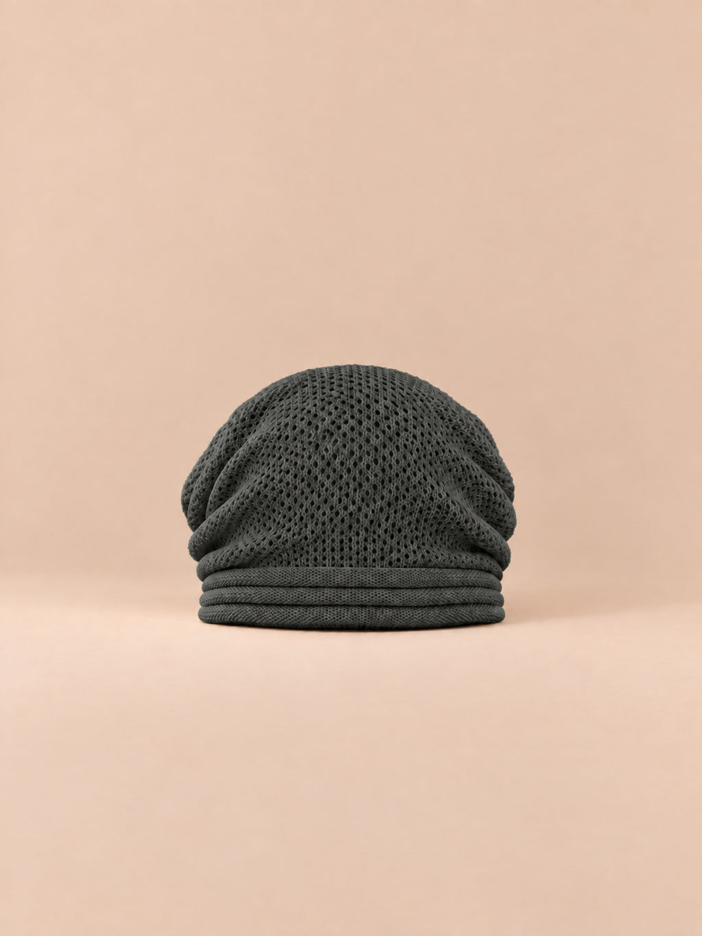 Bonnet oversize en maille gris foncé, vue de face sur fond pêche sable.