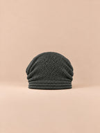Bonnet oversize en maille gris foncé, vue de face sur fond pêche sable.