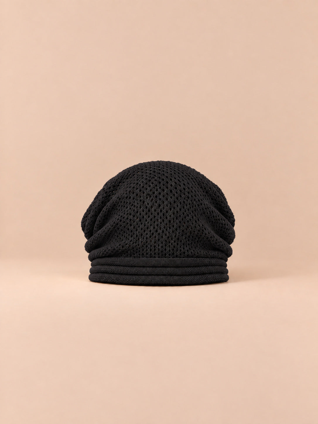 Bonnet oversize en maille noir, vue de face sur fond pêche sable.