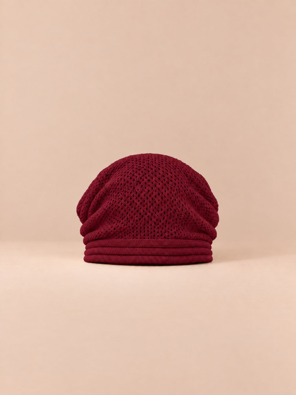 Bonnet oversize en maille rouge, vue de face sur fond pêche sable.