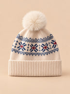 Bonnet cachemire beige à pompon et motif nordique, vue de face sur fond pêche sable
