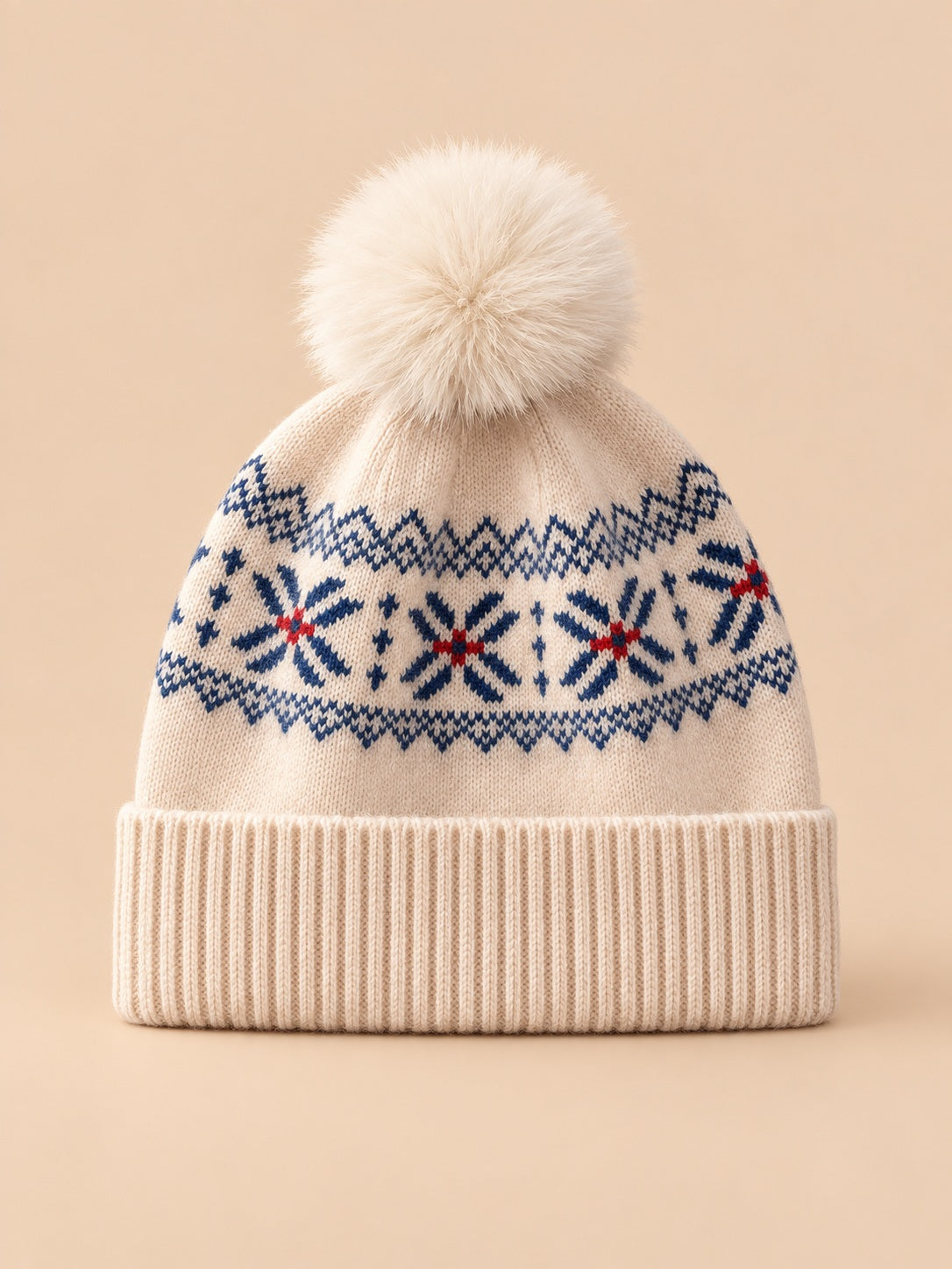 Bonnet cachemire beige à pompon et motif nordique, vue de face sur fond pêche sable