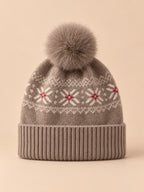 Bonnet cachemire camel à pompon et motif nordique, vue de face sur fond pêche sable