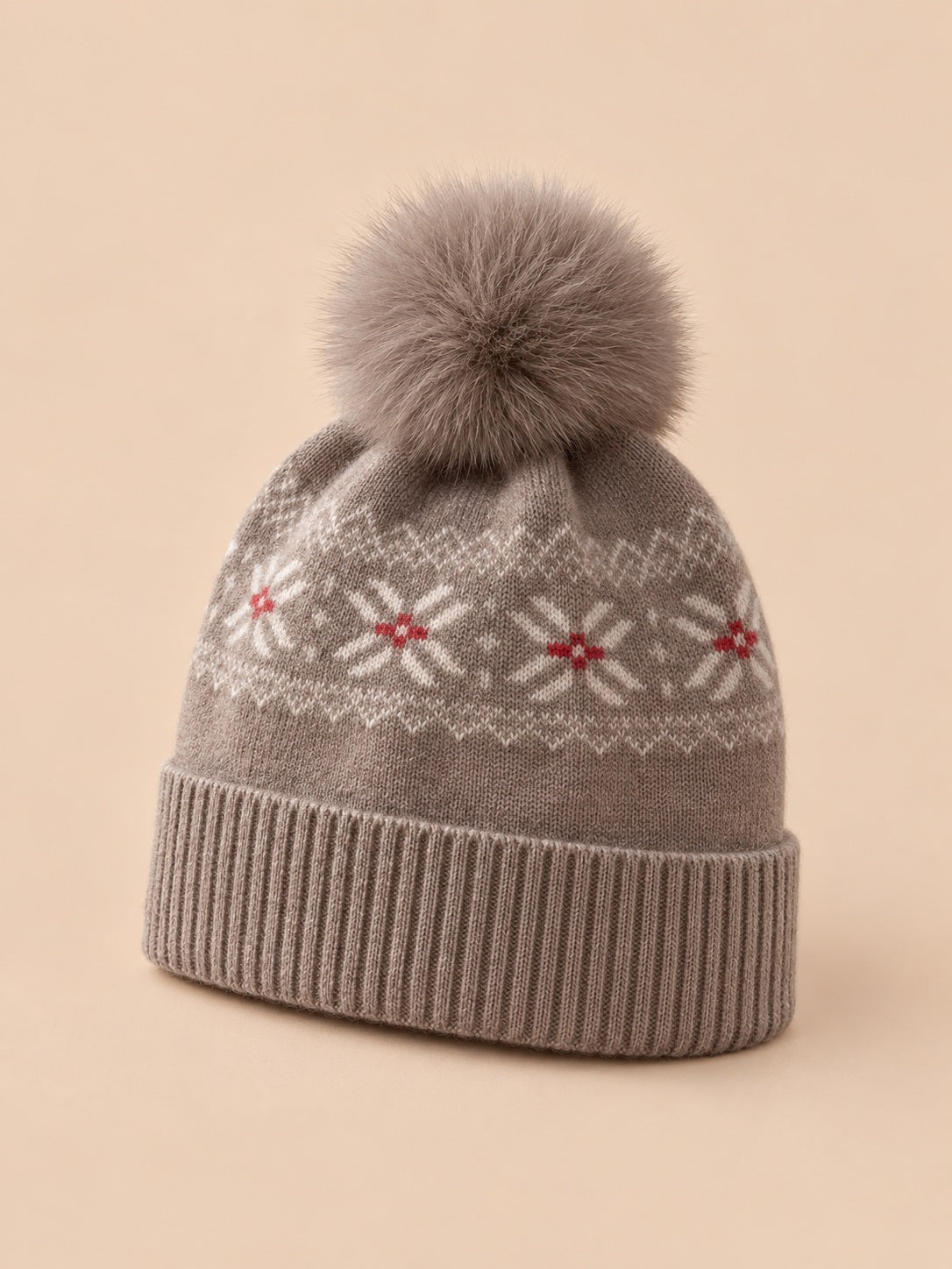 Bonnet cachemire camel à pompon et motif nordique, vue trois quarts sur fond pêche sable