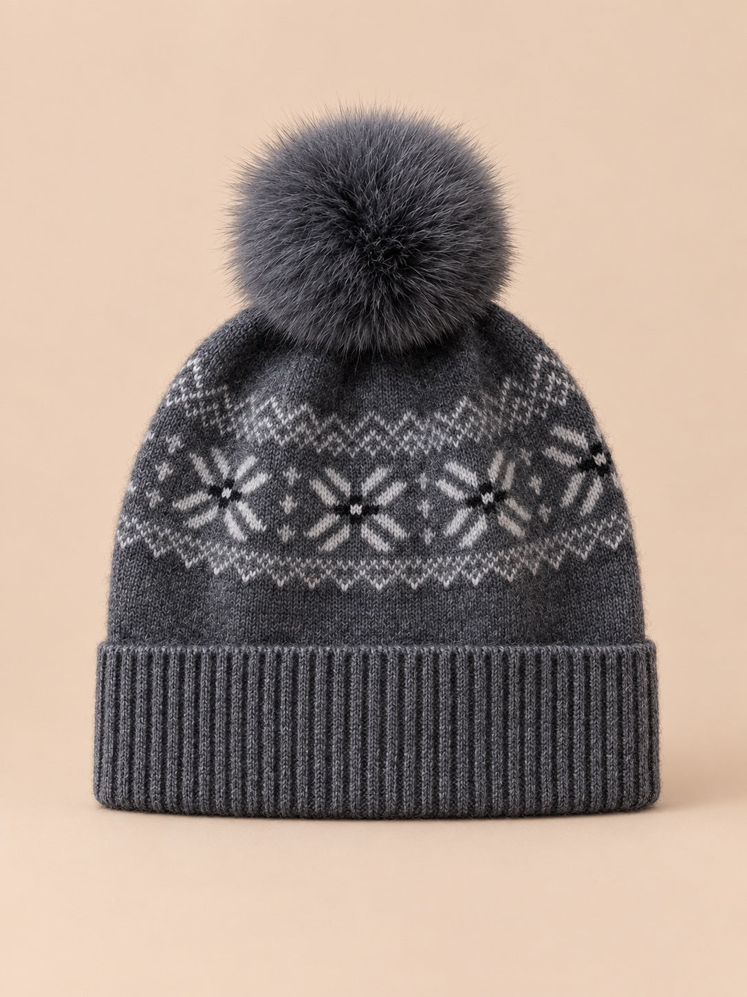Bonnet cachemire gris foncé à pompon et motif nordique, vue de face sur fond pêche sable