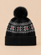 Bonnet cachemire noir à pompon et motif nordique, vue de face sur fond pêche sable