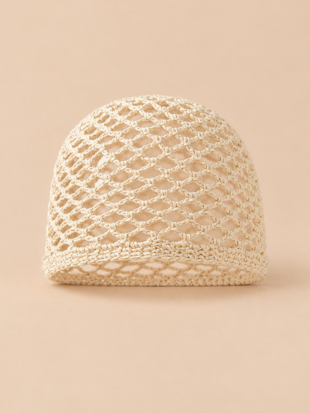 Bonnet fin femme beige en coton résille ajouré, vue de face sur fond pêche sable