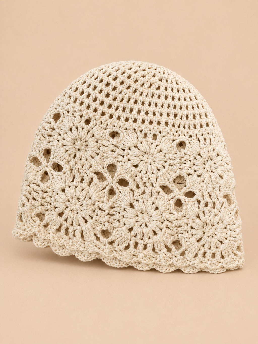 Bonnet turban femme beige ajouré à fleurs au crochet, vue de face sur fond pêche sable