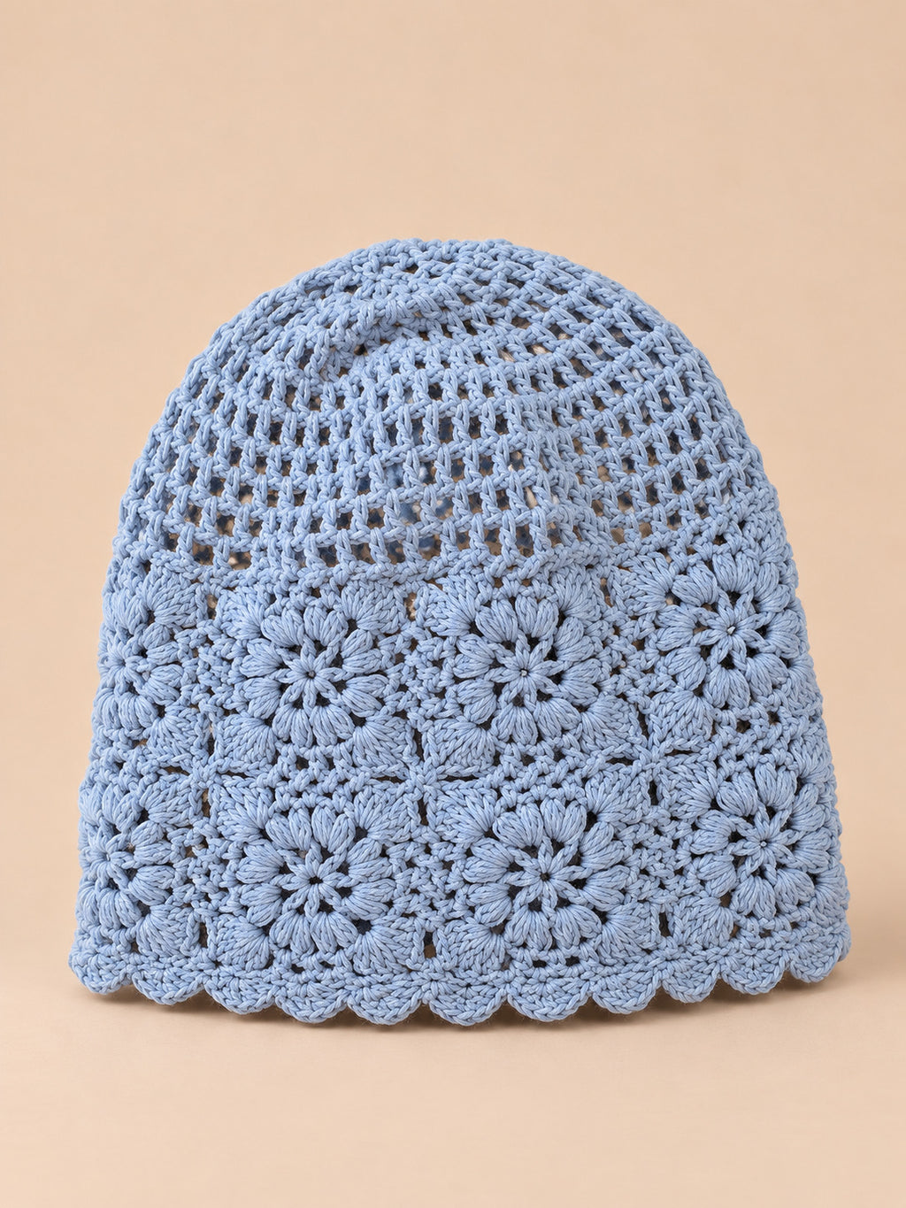 Bonnet turban femme bleu ajouré à fleurs au crochet, vue de face sur fond pêche sable