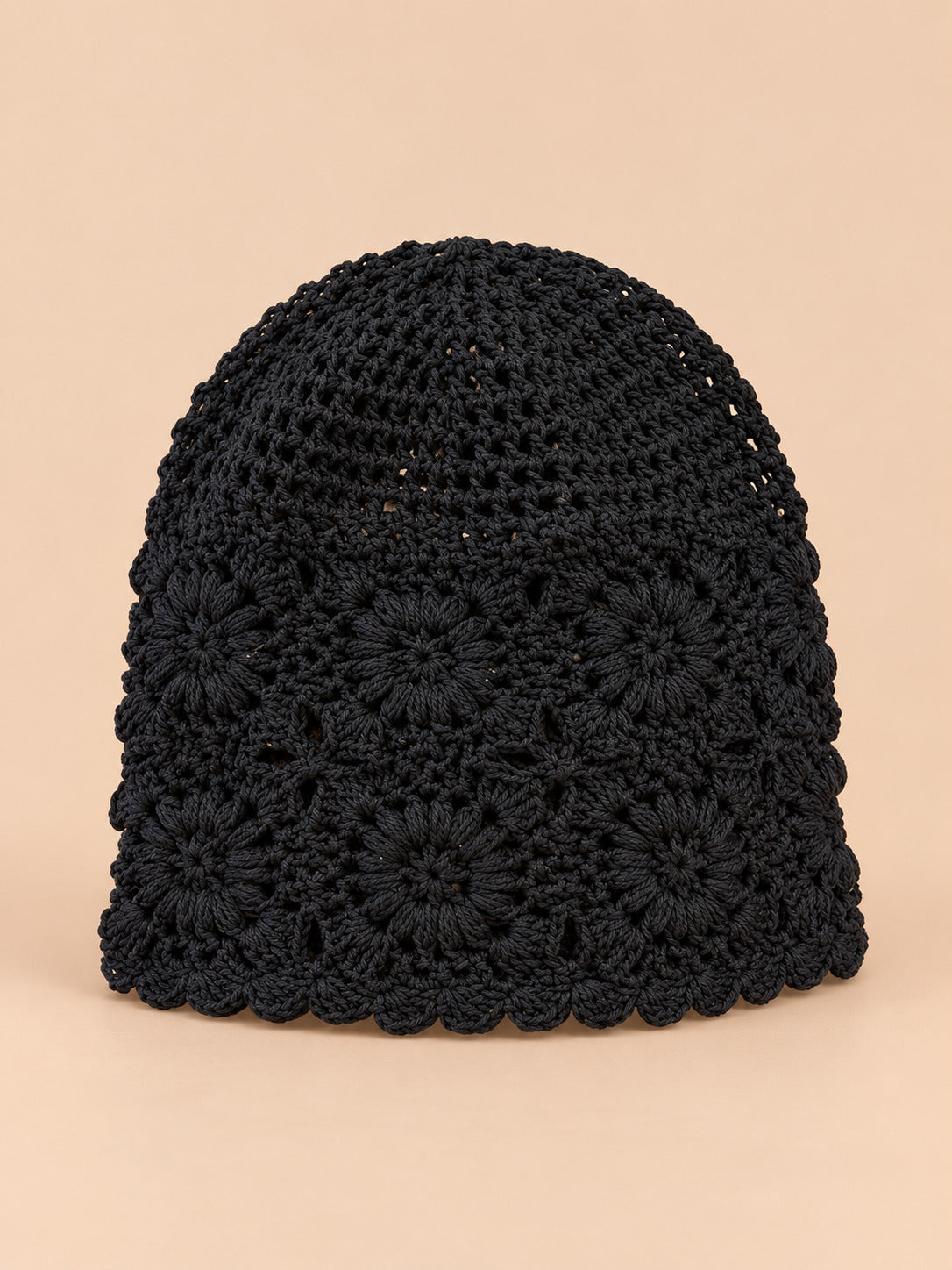 Bonnet turban femme noir ajouré à fleurs au crochet, vue de face sur fond pêche sable