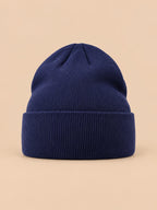 Bonnet uni classique en maille bleu marine, vue de face sur fond pêche sable