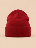 Bonnet uni classique en maille bordeaux, vue de face sur fond pêche sable