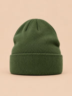 Bonnet uni classique en maille vert, vue de face sur fond pêche sable